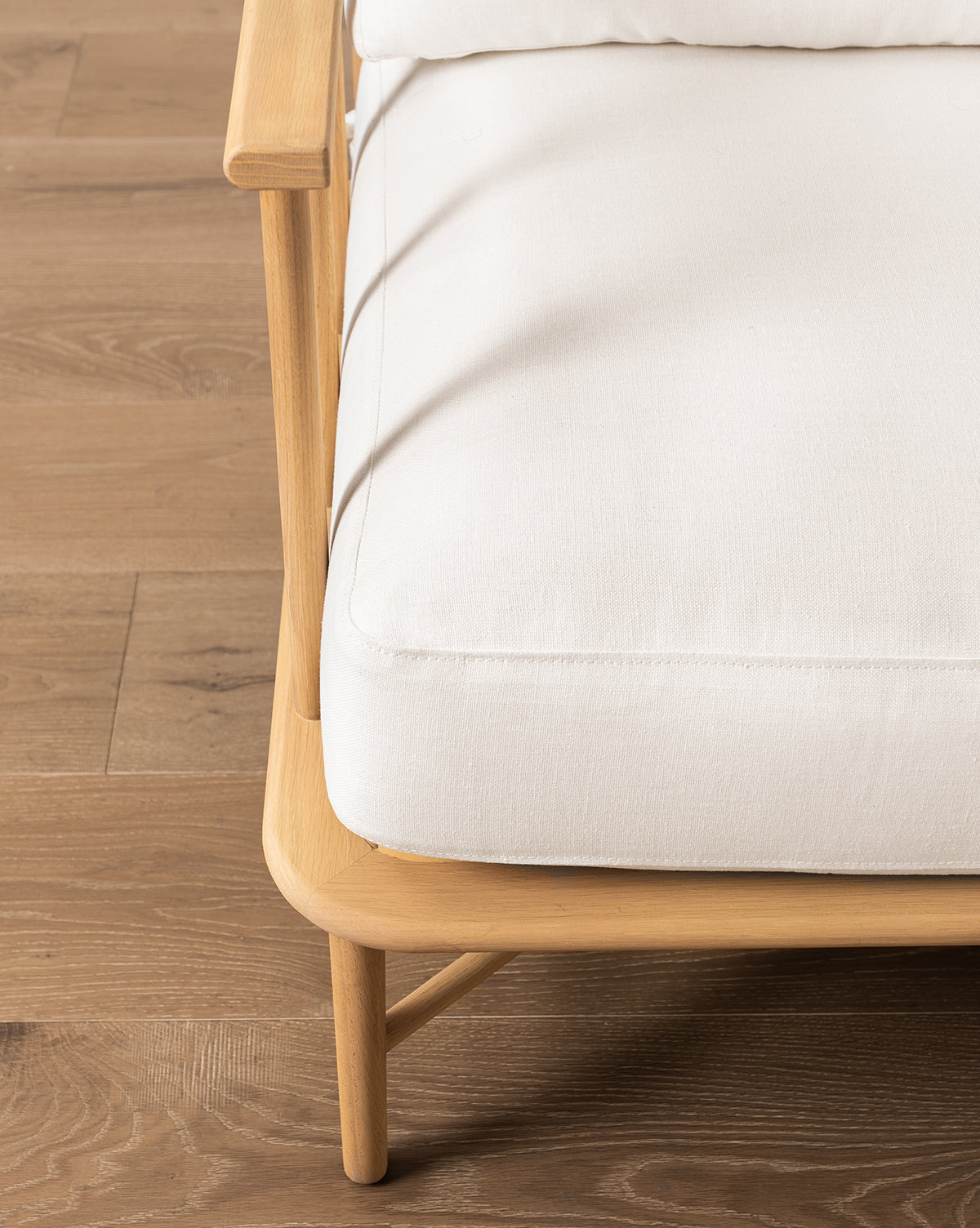 A close-up of the Alma Lounge Chair, with white cushions and a solid oak frame on a wooden floor, by McGee & Co.