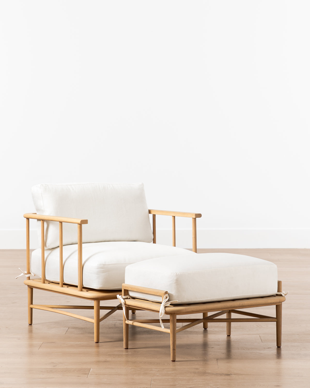 The Alma Lounge Chair, featuring plush cushions and a matching ottoman, stands on a light wood floor against a plain white wall, emphasizing its modern design by McGee & Co.