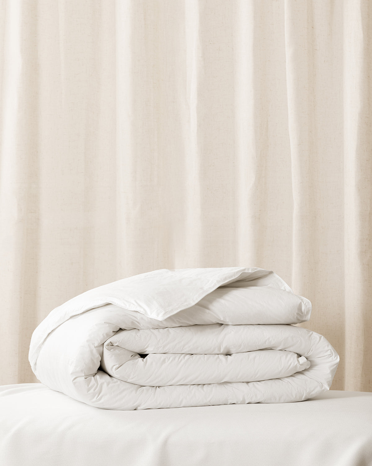 A folded white duvet insert on a bed with a window curtain in the background from McGee & Co.