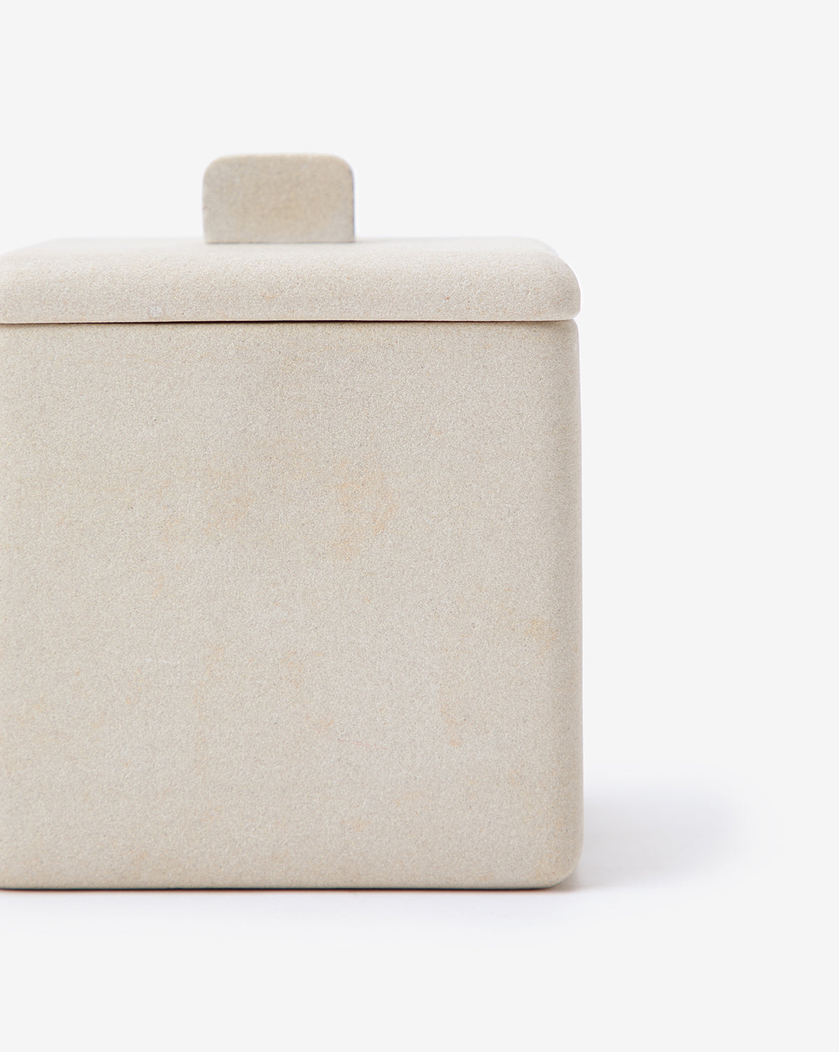 A close-up of the Amada Sandstone Bath Collection’s beige square container with a matching lid and small handle adds an organic touch to bathroom decor, set against a plain white background.