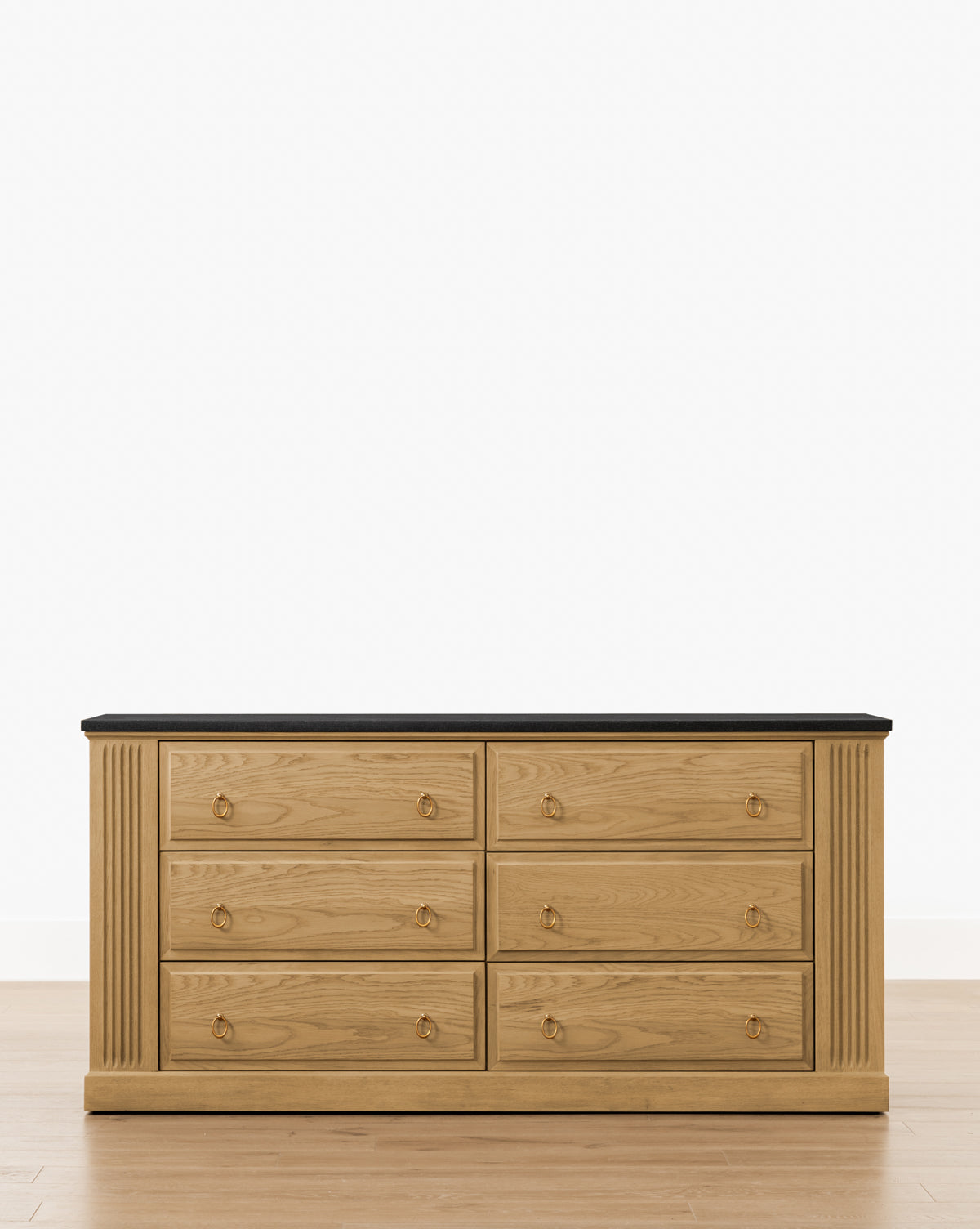 An Ambrose Dresser by YANG CHENG WOODEN INDUSTRIES INTERNATIONAL (VIETNAM) CO LTD features six drawers, solid brass drop pulls, vertical fluted side accents, and a dark flat top, shown on a light wood floor against a white background. McGee & Co.