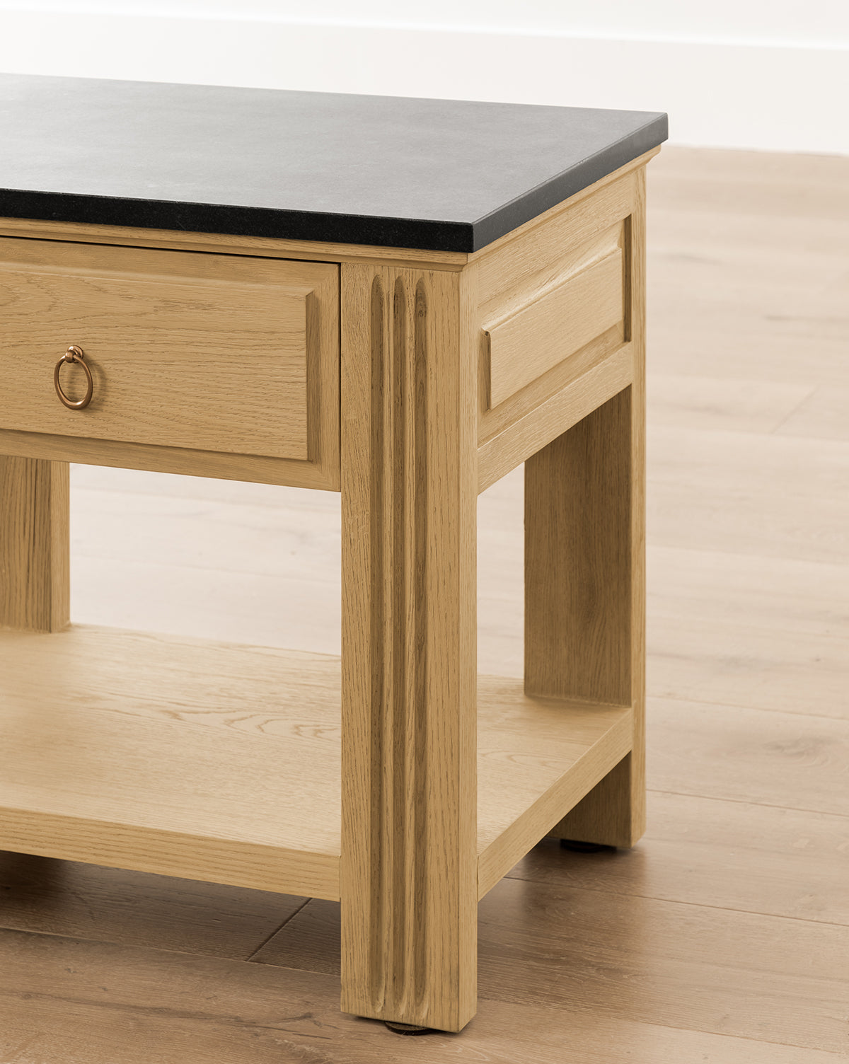 A close-up of the Ambrose Nightstand, featuring a black tabletop, single drawer with round metal handle, fluted legs, and an open lower shelf. It sits on a wooden floor, bringing vintage bedroom charm to the space by McGee & Co.