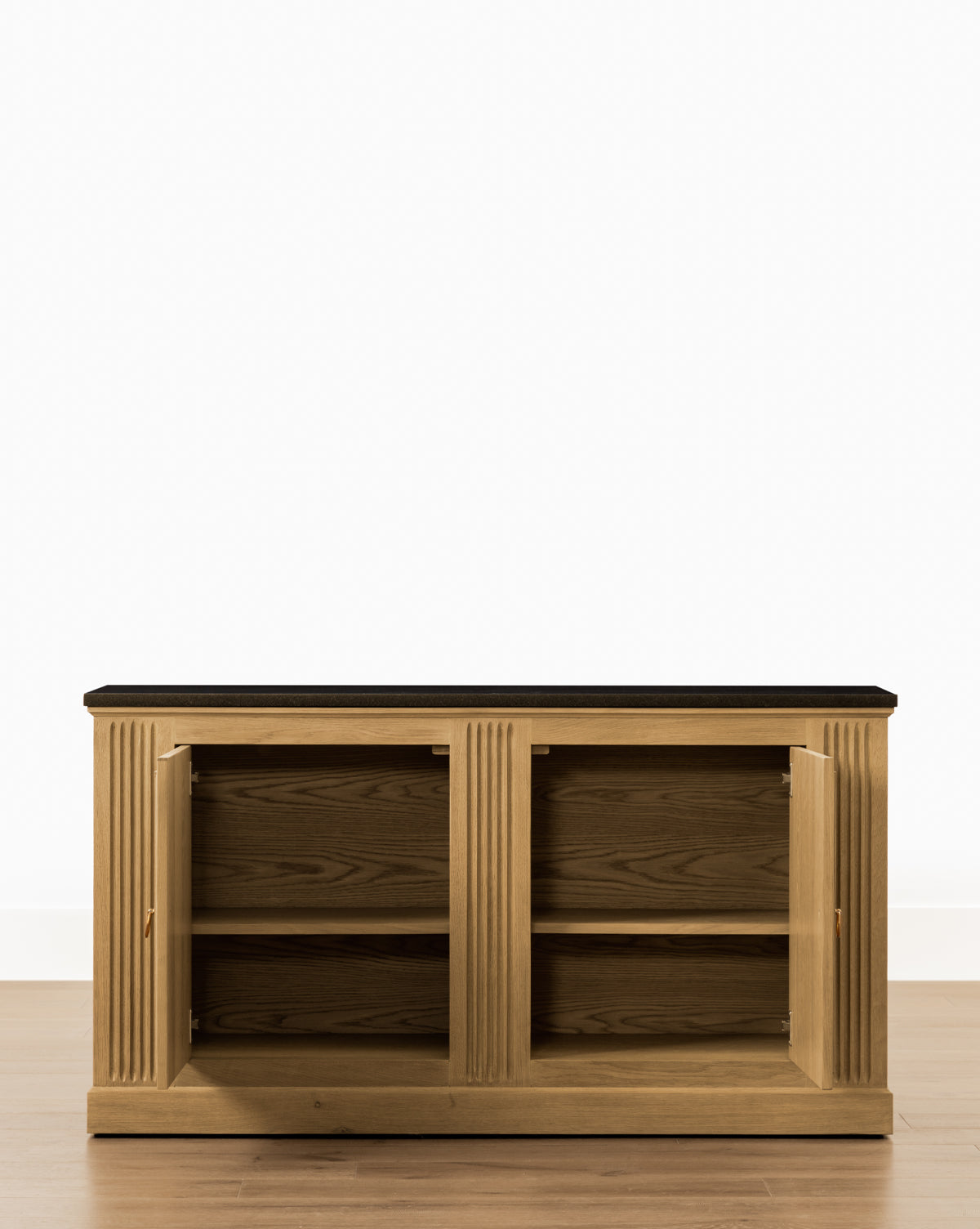 The Ambrose Sideboard features a dark top and two open doors revealing two interior shelves, by McGee & Co. This vintage piece sits on a light wooden floor against a plain white wall.