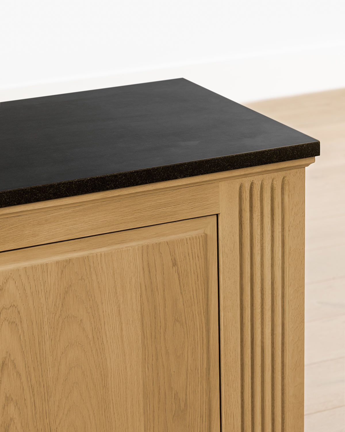 A close-up of the Ambrose Sideboard featuring fluted detailing and a flat black countertop, set against a light-colored wall and floor, by McGee & Co.