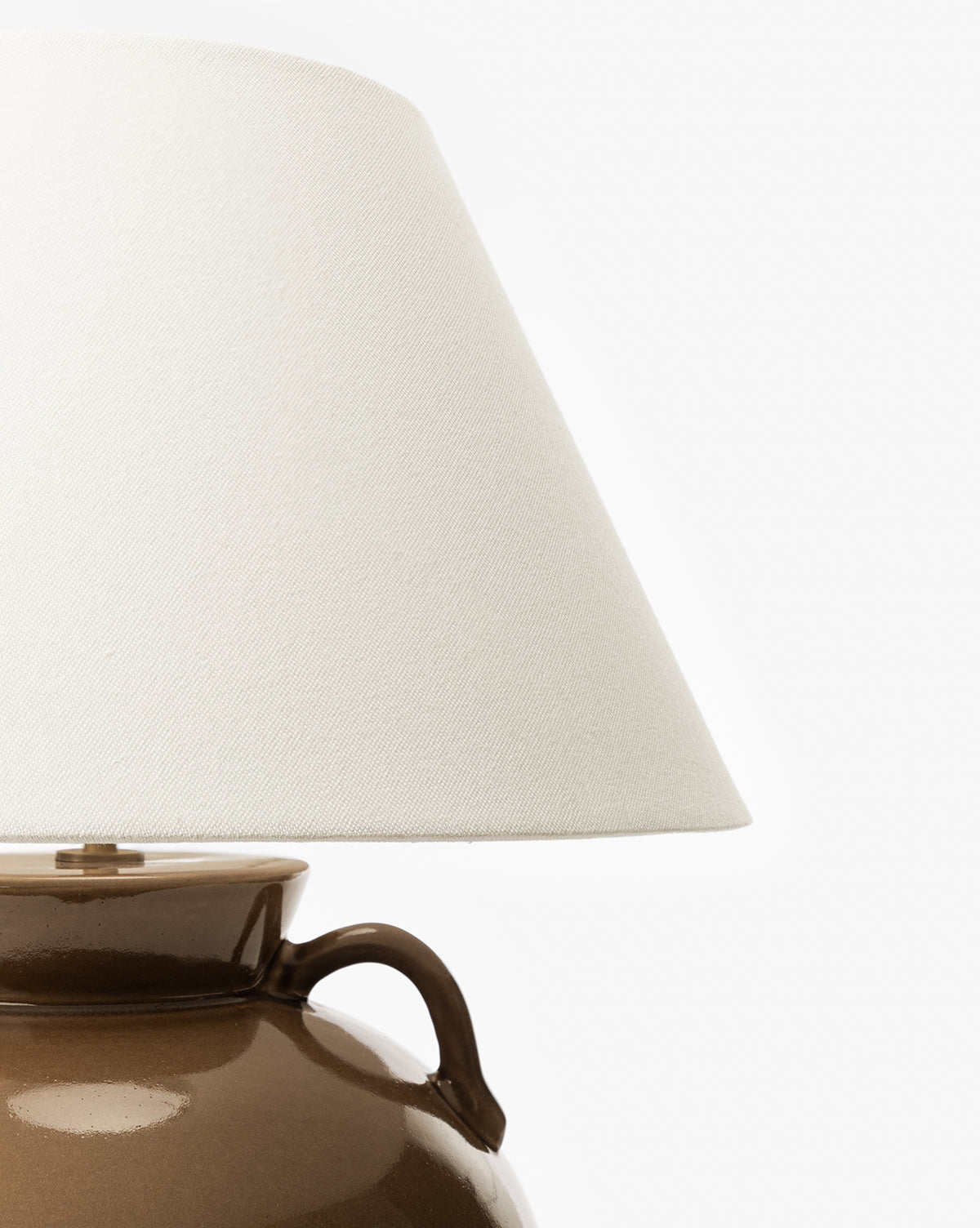 A close-up of the Amphora Table Lamp highlights its brown ceramic base and white fabric shade, with only the upper part of the lamp and lower portion of the shade visible against a plain white background, by McGee & Co.