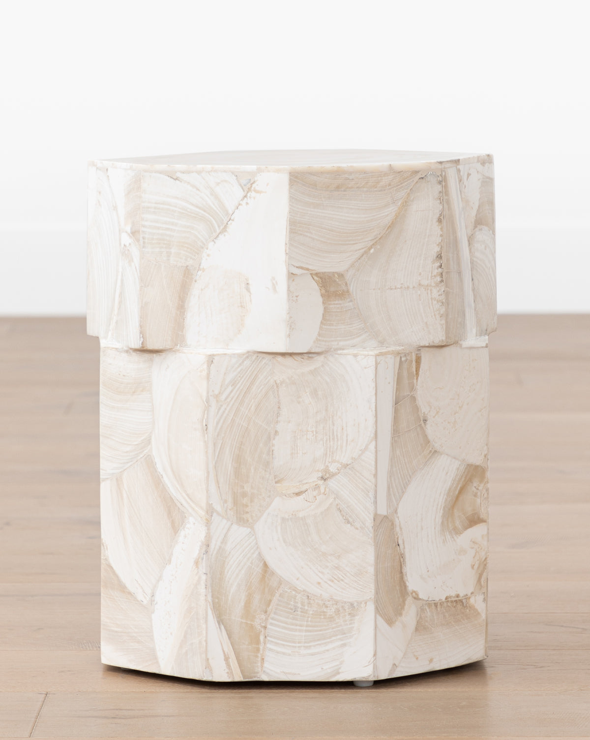 The Andrade Side Table by JANICE MINOR EXPORT, INC. features a round, contemporary design with textured beige and white brushstroke patterns, displayed on a wooden floor against a plain white background by McGee & Co.