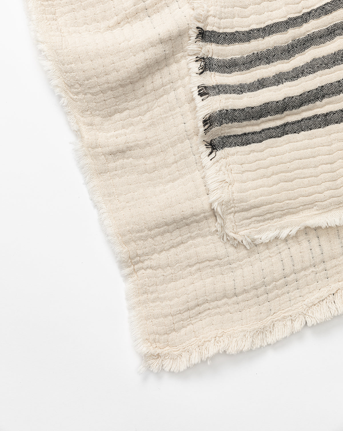 The Anneliese Striped Throw by Creative Co-op, with cream and black stripes, textured cotton, and fringe trim, is elegantly layered with a matching cream throw on a white backdrop for a luxe home decor look by McGee & Co.