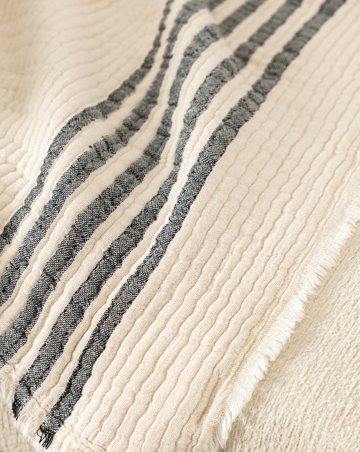 The Anneliese Striped Throw by Creative Co-op features cream-colored, textured cotton with three black stripes, a wavy quilted look, and slightly frayed edges—ideal for adding a luxurious accent to your home decor. McGee & Co.