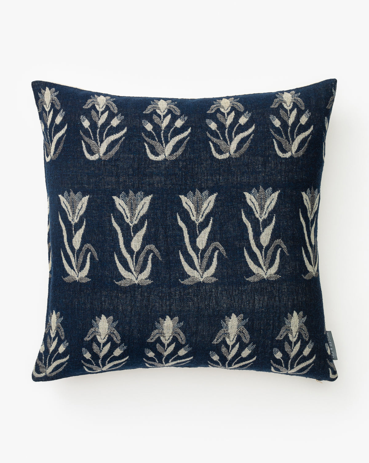 The Annika Pillow Cover is a square, navy blue cover with light beige floral motifs in horizontal rows, made from a luxurious wool and silk blend, by McGee & Co.
