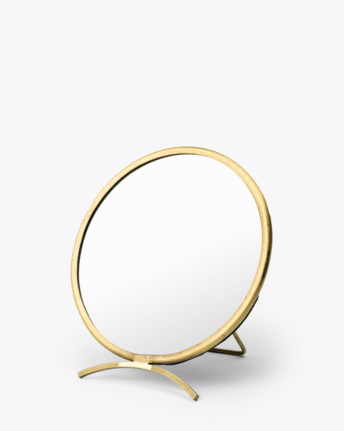 The Antique Brass Folding Mirror is a round tabletop dresser mirror with a brass-finished frame and stand, shown at a slight angle on a plain white background by McGee & Co.