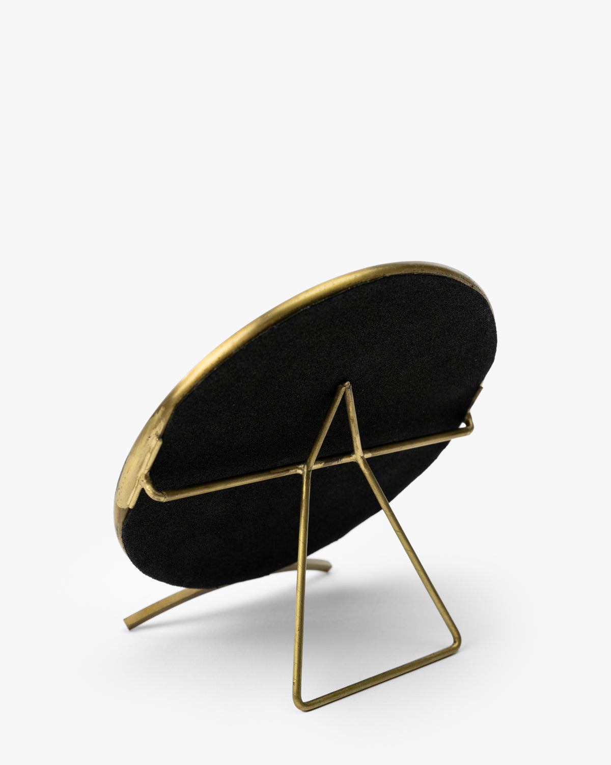 A round photo frame with a brass-finished frame and stand, shown from the back with black backing on a white background—ideal for pairing with your dresser mirror or the Antique Brass Folding Mirror, by McGee & Co.