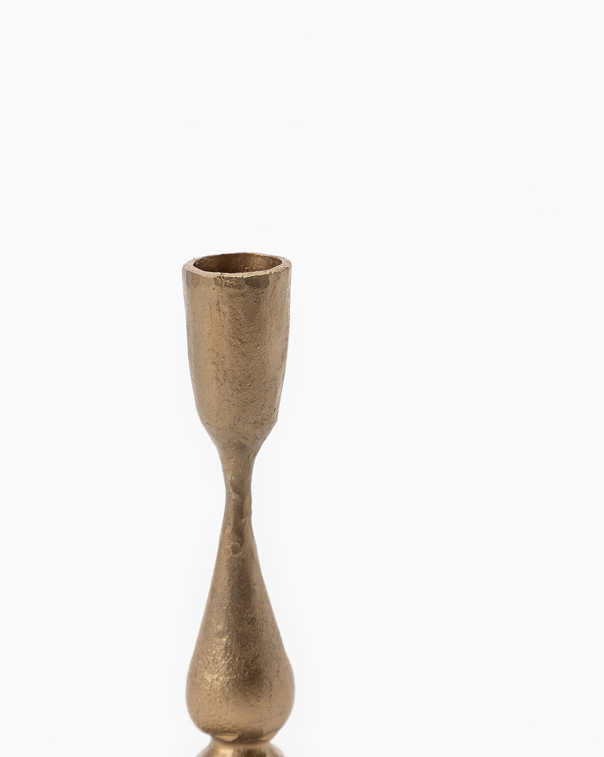 The Antique Brass Taper Candle Holder, featuring a textured surface, narrow stem, and rounded base, sits slightly left of center on a plain white background. Its brass finish gleams softly with ample empty space on the right.