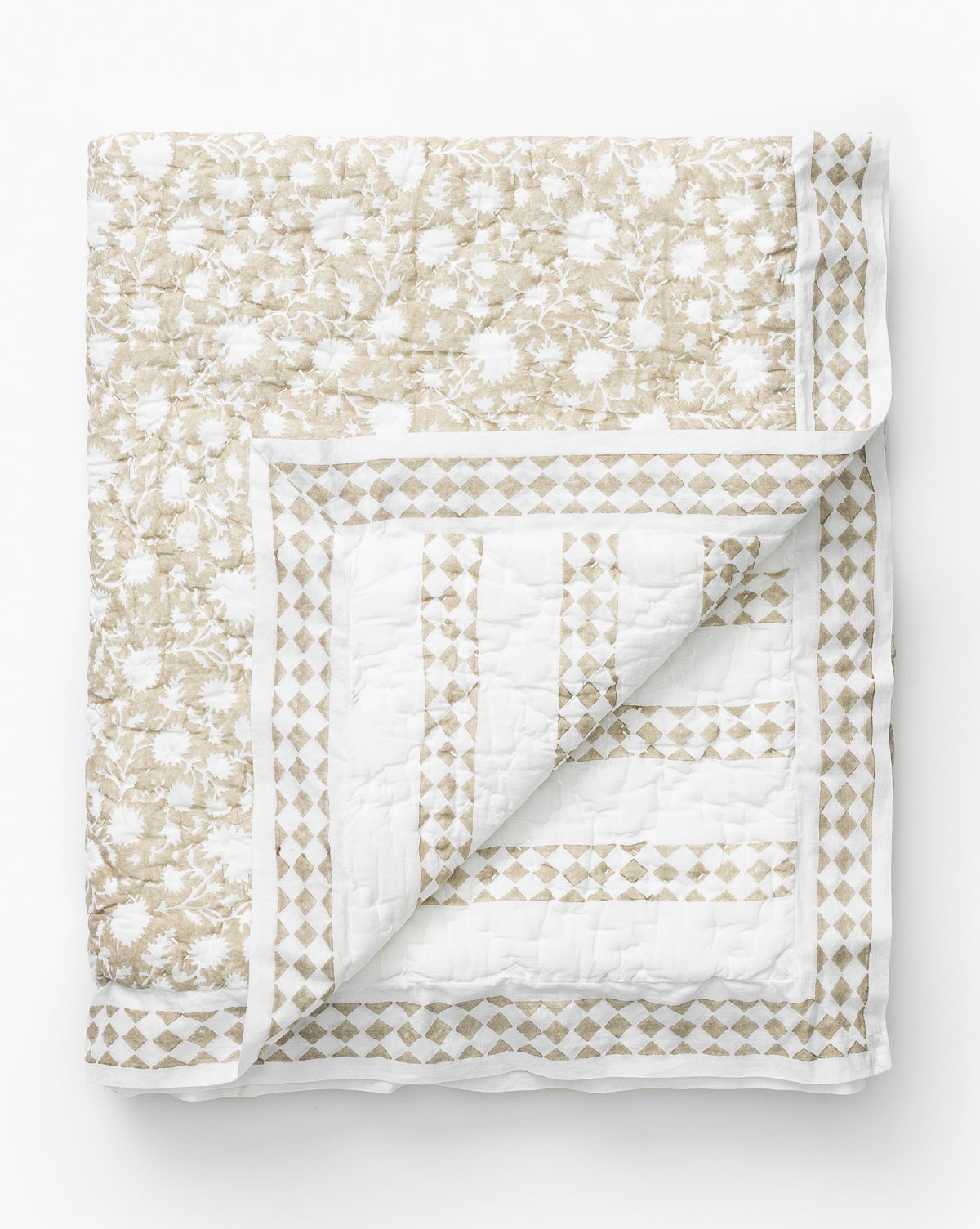 The Arcadia Block Print Kids Quilt features a beige floral pattern on white with a geometric diamond border. A corner is flipped to reveal its matching inner design, all displayed on a white surface for added charm.