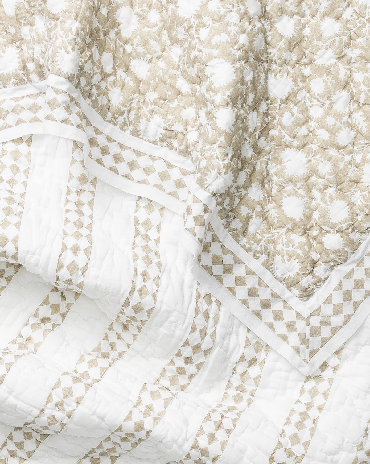 A close-up of the Arcadia Block Print Kids Quilt reveals cream and white floral patterns, a diamond geometric border, and striped quilted sections, combining textures for an intricate and soft design.