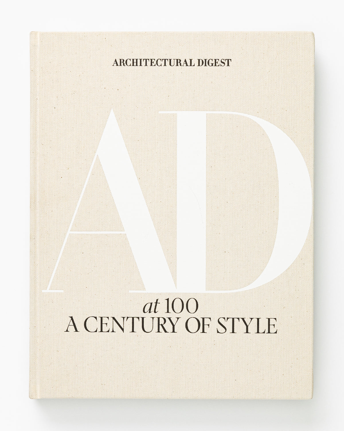 A beige hardcover coffee table book, Architectural Digest at 100, has bold white AD letters and black text on the cover, celebrating a century of iconic design styles.