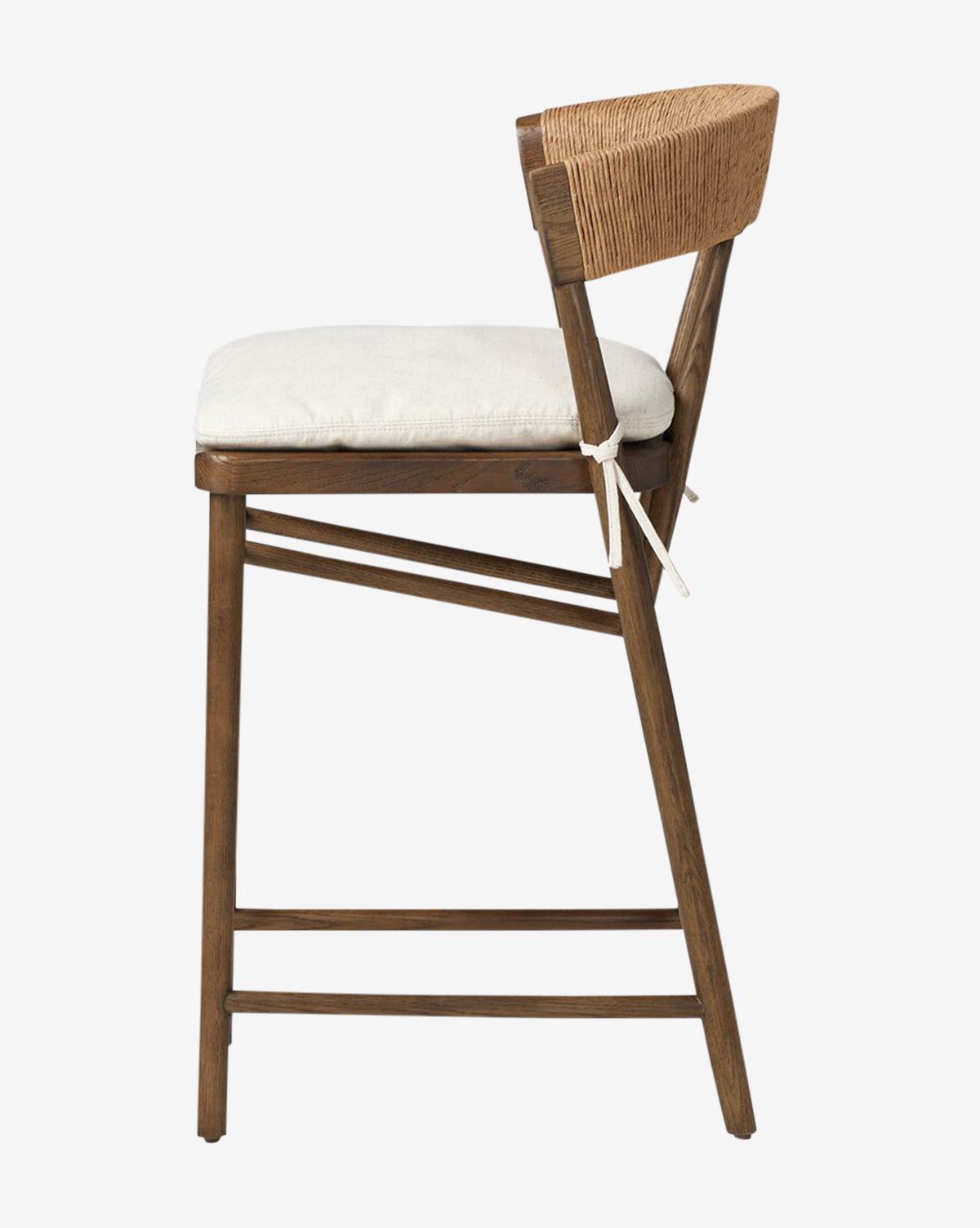 Side view of the Four Hands Ardent Stool, featuring a solid oak frame with angled legs, woven rope backrest, and a light cushioned seat secured with fabric ties—ideal for your kitchen bar. McGee & Co.