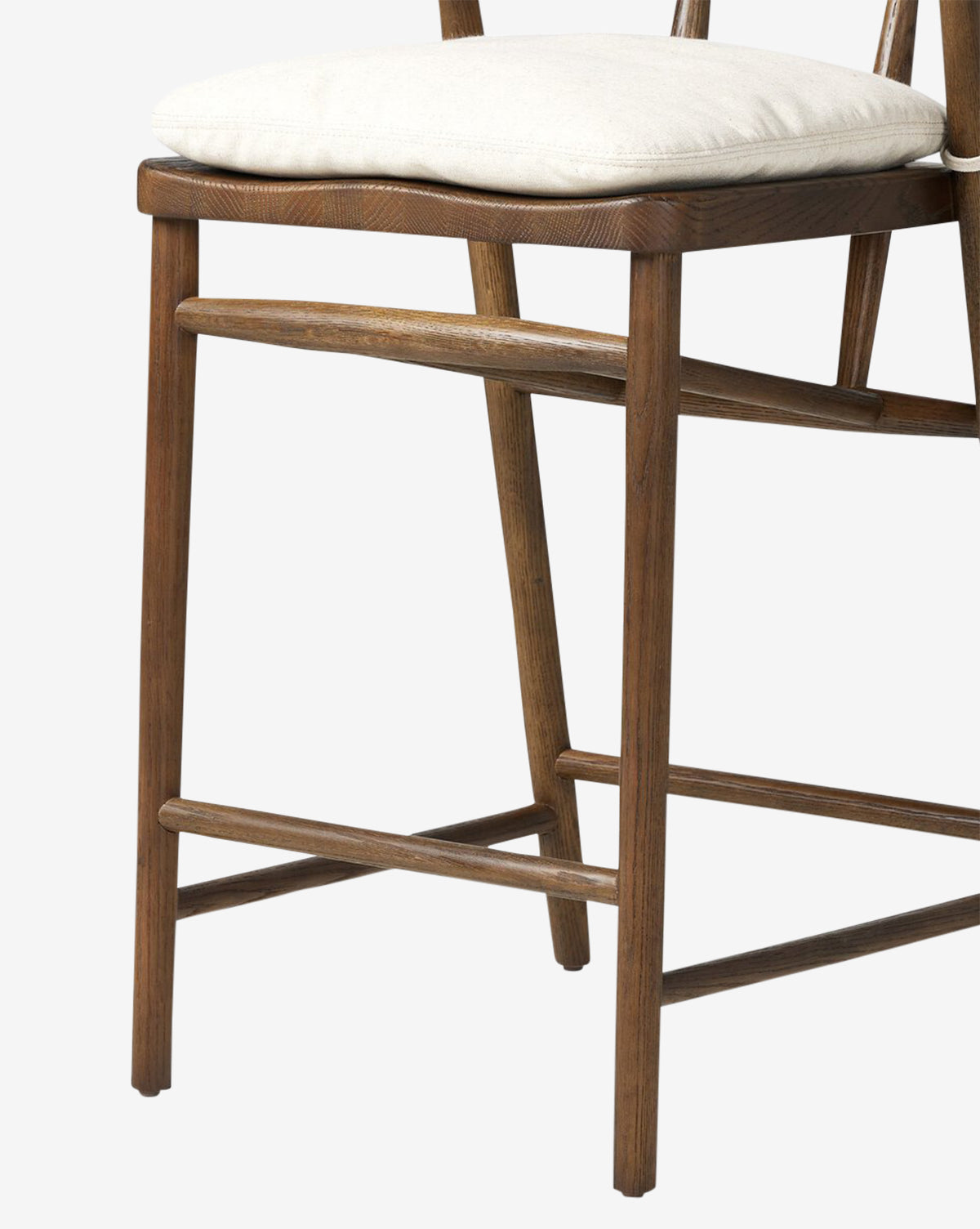 A close-up of the Four Hands Ardent Stool shows its solid oak frame and light cushioned seat, highlighting the legs, seat, and backrest—an ideal addition to any kitchen bar set against a plain background. McGee & Co.