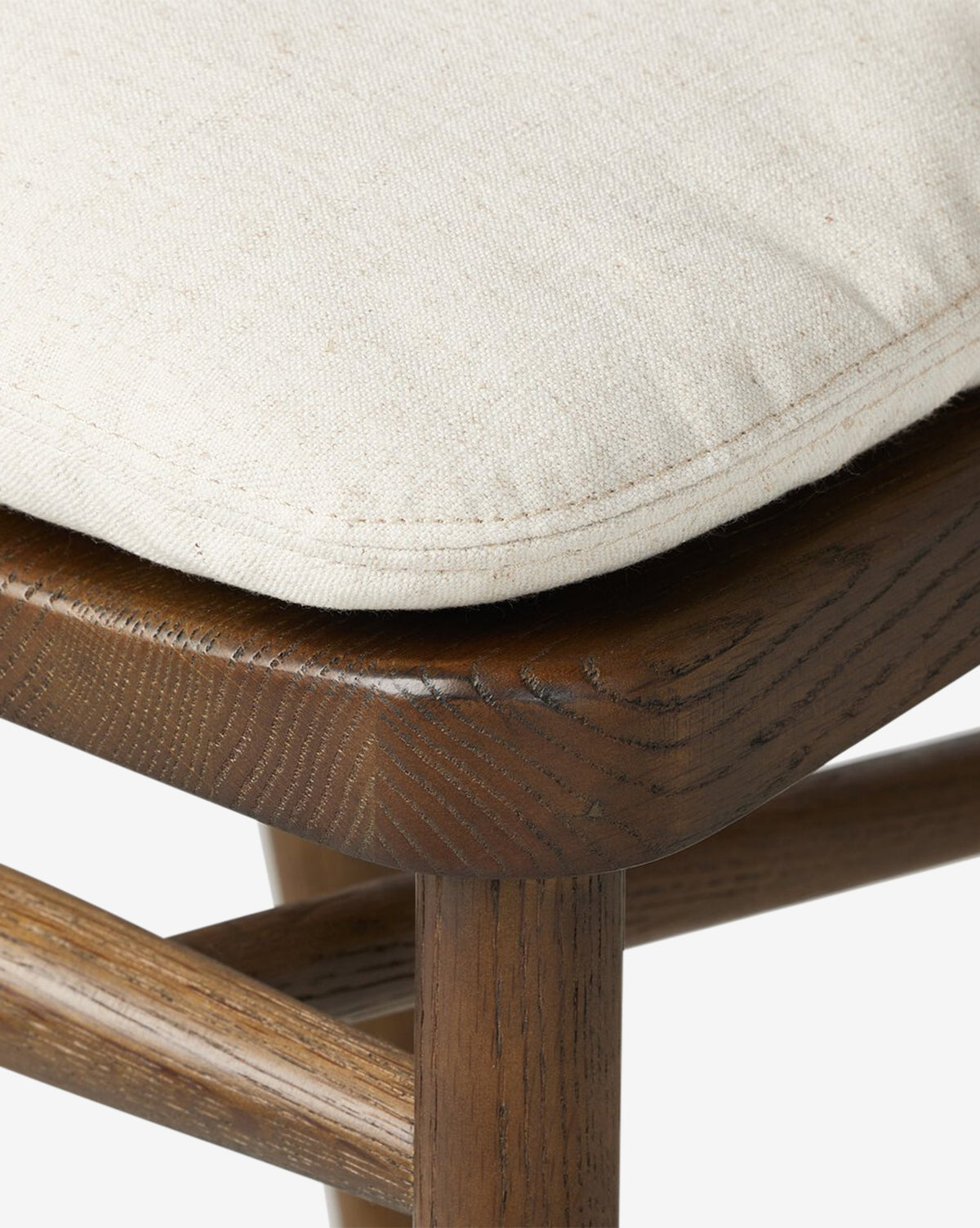 Close-up of the Ardent Stool by Four Hands, showcasing its solid oak frame with visible grain and subtle scratches. The beige upholstered cushion looks soft and textured—an ideal addition to any kitchen bar. McGee & Co.