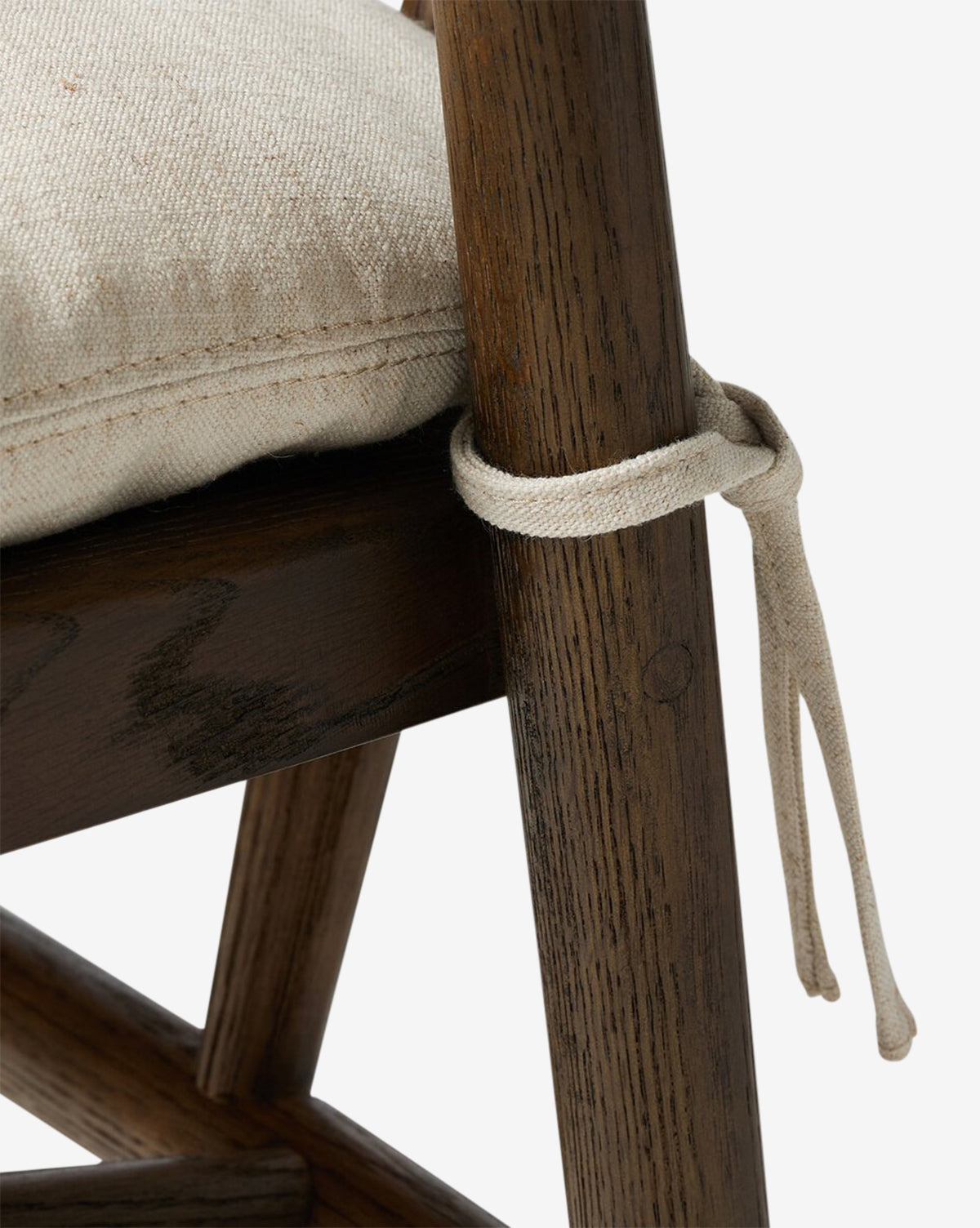 Close-up of the Four Hands Ardent Stool, featuring a solid oak frame with a dark finish and a light, textured cushion tied to the chair back—perfect for bringing comfort and style to any kitchen bar. McGee & Co.