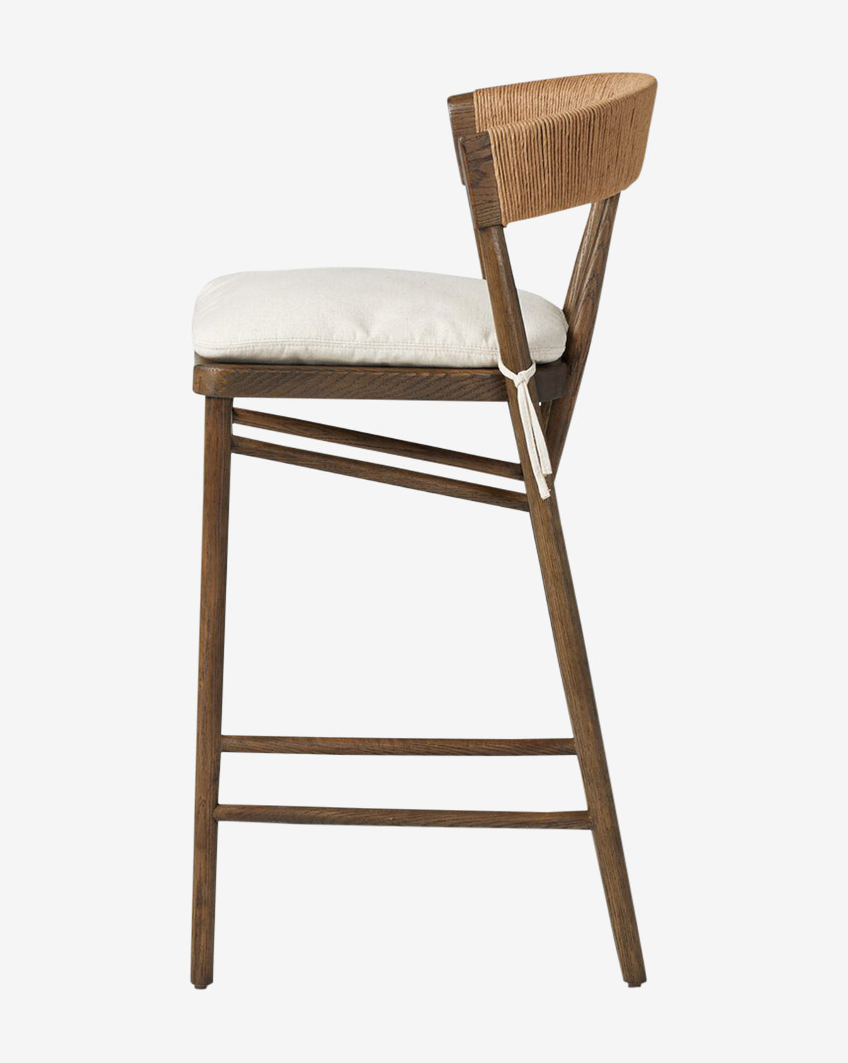 Side view of the Ardent Stool by Four Hands, featuring an oak frame, light cushioned seat, and woven paper rush backrest. Angled legs with horizontal supports offer a modern, minimalist look. McGee & Co.