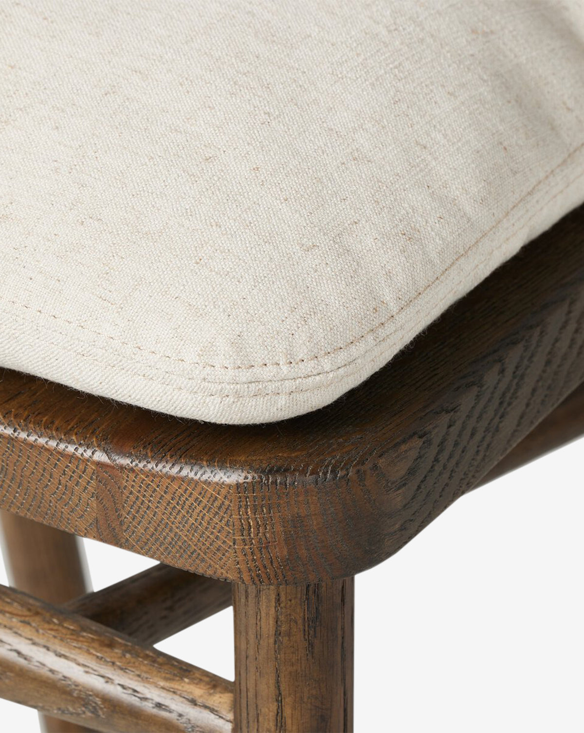 The Ardent Stool by Four Hands features a solid oak frame, dark wood grain, and a light beige textured cushion with detailed stitching—adding refined charm to any kitchen bar. McGee & Co.