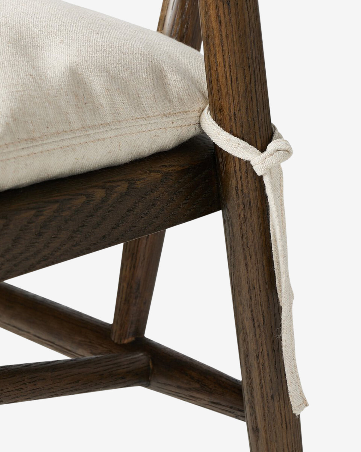 Close-up of the Four Hands Ardent Stool, showcasing its dark solid oak frame and seat with a textured beige cushion, secured by a fabric strap—McGee & Co.
