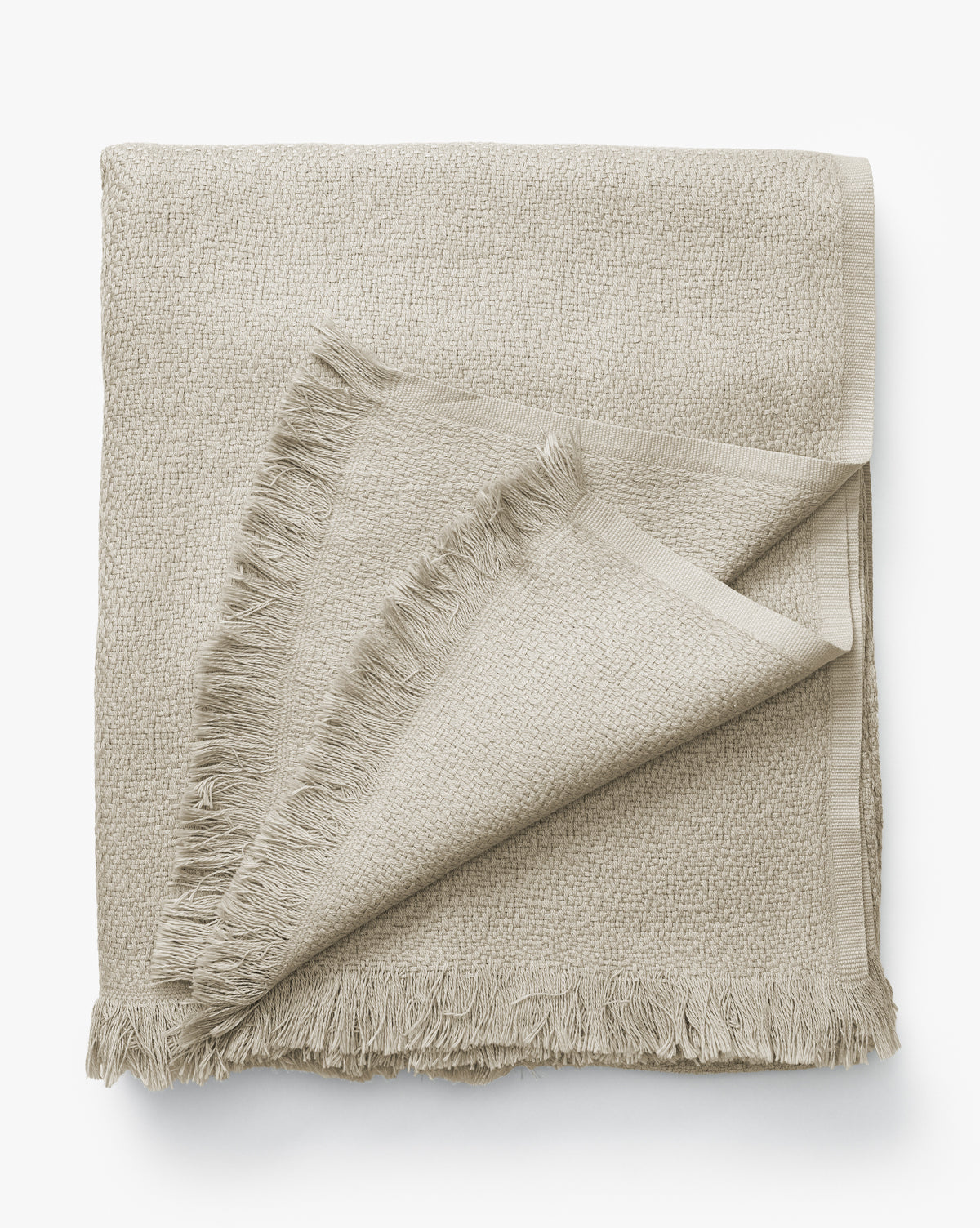 The Ariella Throw by J Call Designs LLC dba Sew Miami LLC is a light beige cotton throw with fringed edges and subtle texture, shown neatly folded on a white background—ideal for enhancing a neutral color scheme. McGee & Co.