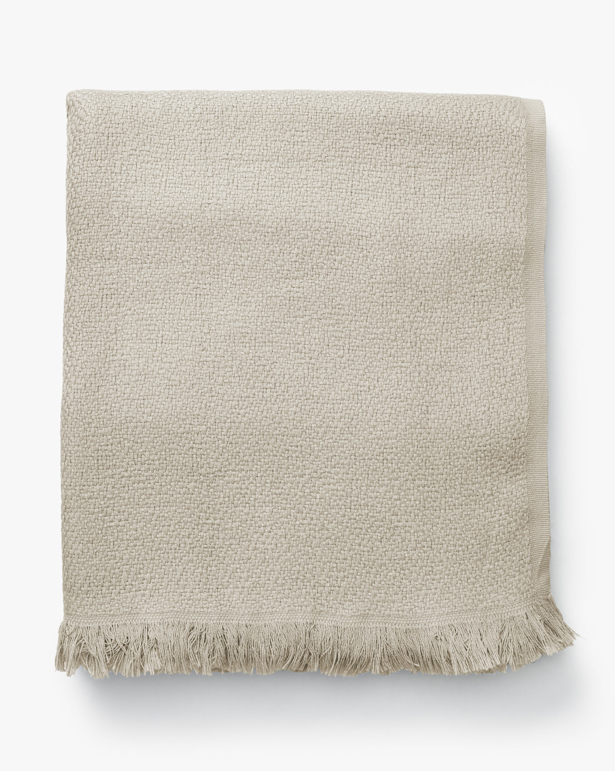 The Ariella Throw by J Call Designs LLC dba Sew Miami LLC is a folded beige cotton throw with a textured finish and short fringe, shown on a white background—ideal for adding warmth to any neutral decor. McGee & Co.