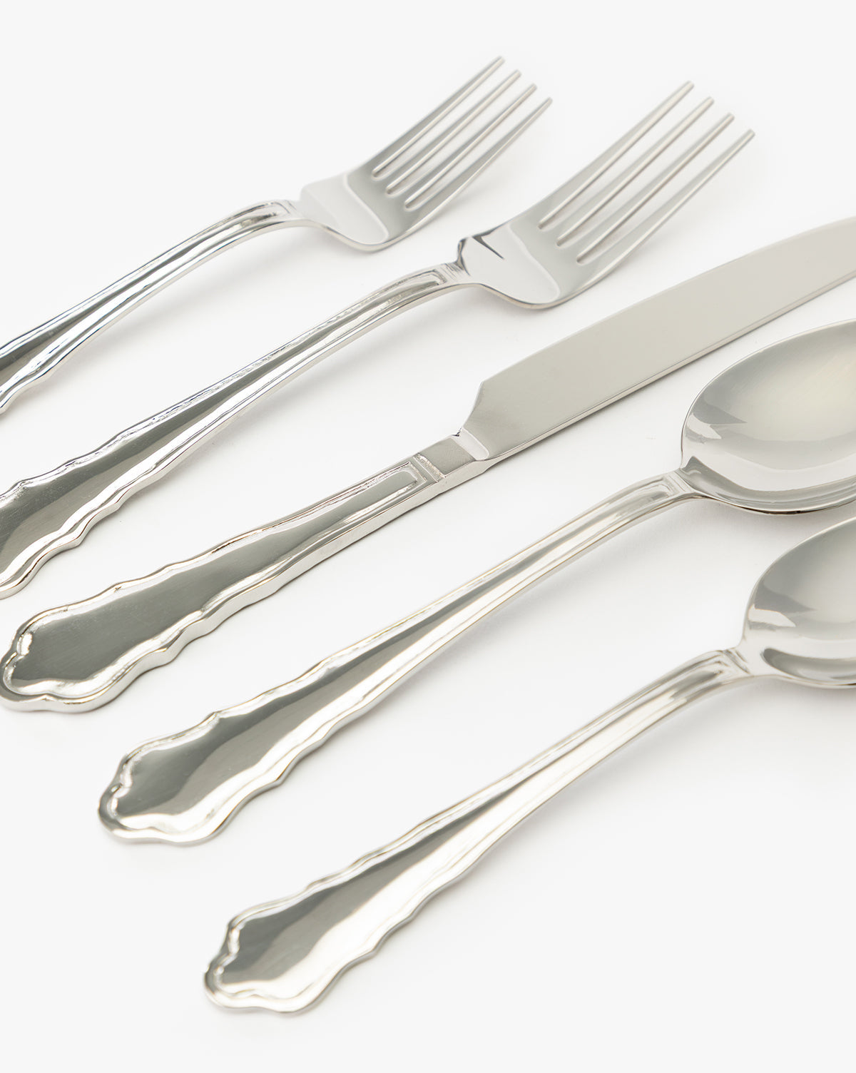 The Artois Flatware (Set of 5) features vintage-inspired pieces—two forks, a knife, and two spoons—each with elegant scalloped edge handles, artfully arranged diagonally on a white background by McGee & Co.