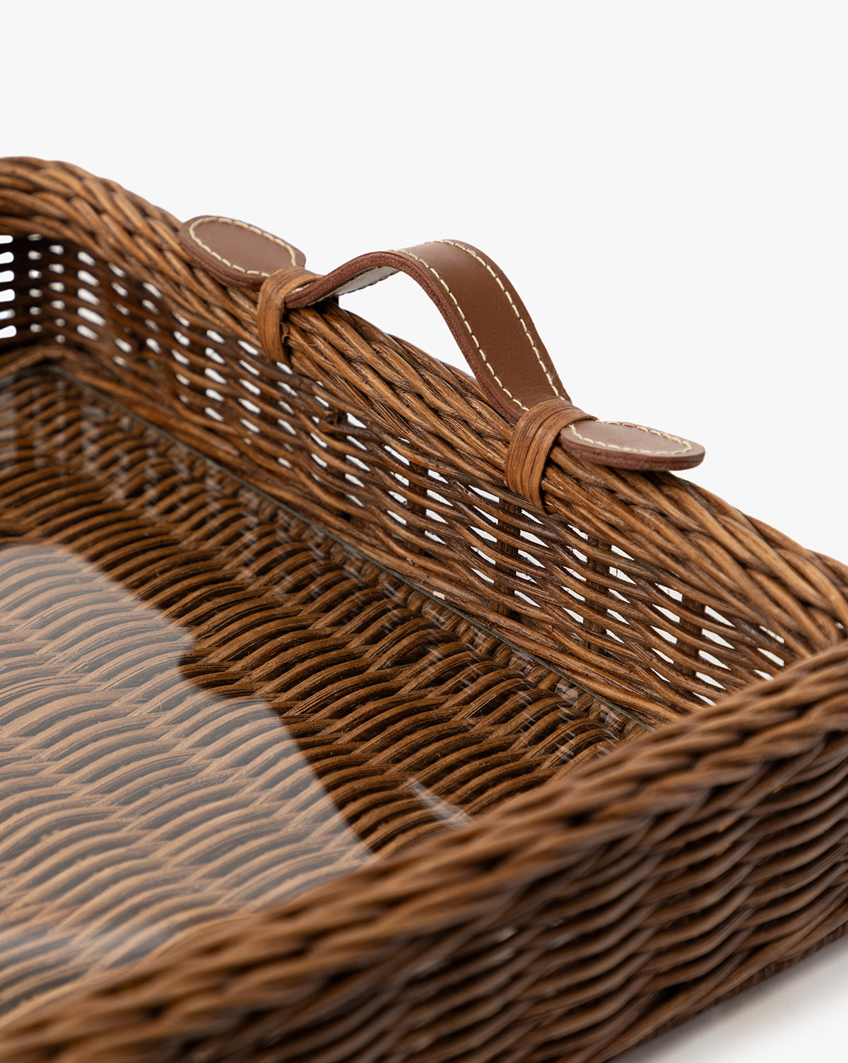 A close-up of the Ashcroft Wicker Tray—a rectangular woven basket with a brown leather handle on one side—set against a plain white background, highlighting the detailed wicker texture, by McGee & Co.
