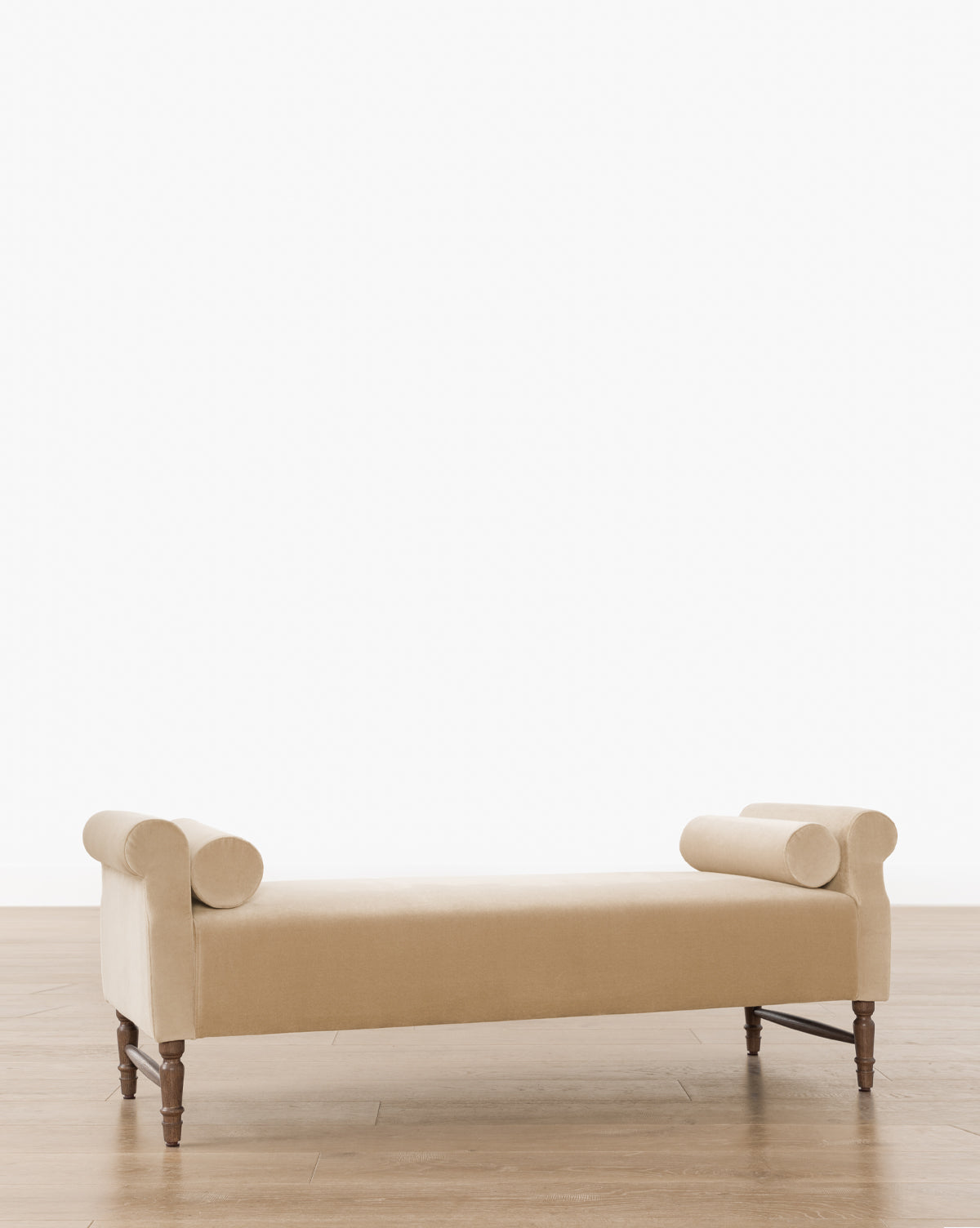 The Asher Bench showcases a beige upholstered seat, striped linen bolster pillows on each end, and wooden legs, all in a sleek modern design, by McGee & Co. It’s pictured on a light wood floor with a plain white background.