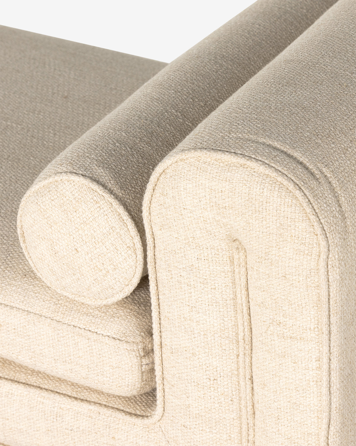 A close-up of the beige textured sofa’s arm and cushion, with a cylindrical bolster pillow and soft edges—features that pair perfectly with the contemporary upholstered Ashlyn Bench in your living space, by McGee & Co.