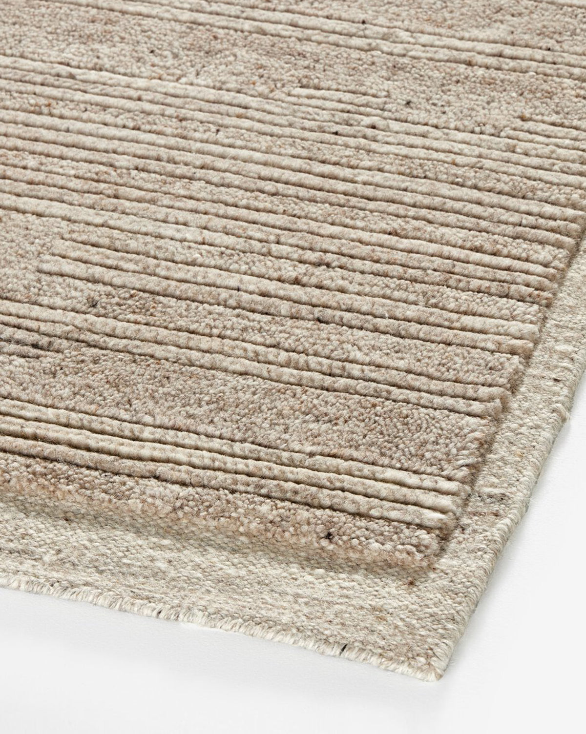 A close-up of the Ashwin Hand-Knotted Wool Rug shows its beige, textured wool surface with horizontal raised stripes, neatly finished edges, and a neutral palette resting on a white background, by McGee & Co.