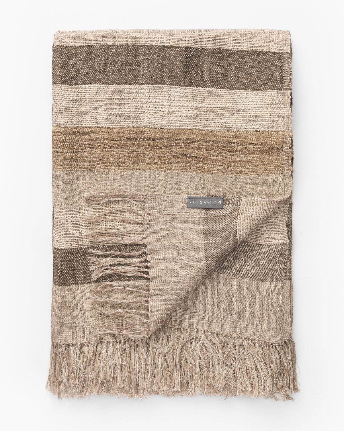 The Ashwood Throw features wide horizontal stripes in brown and beige, fringe edges, and a visible fabric label—making it a stylish decorative accent for your sofa.