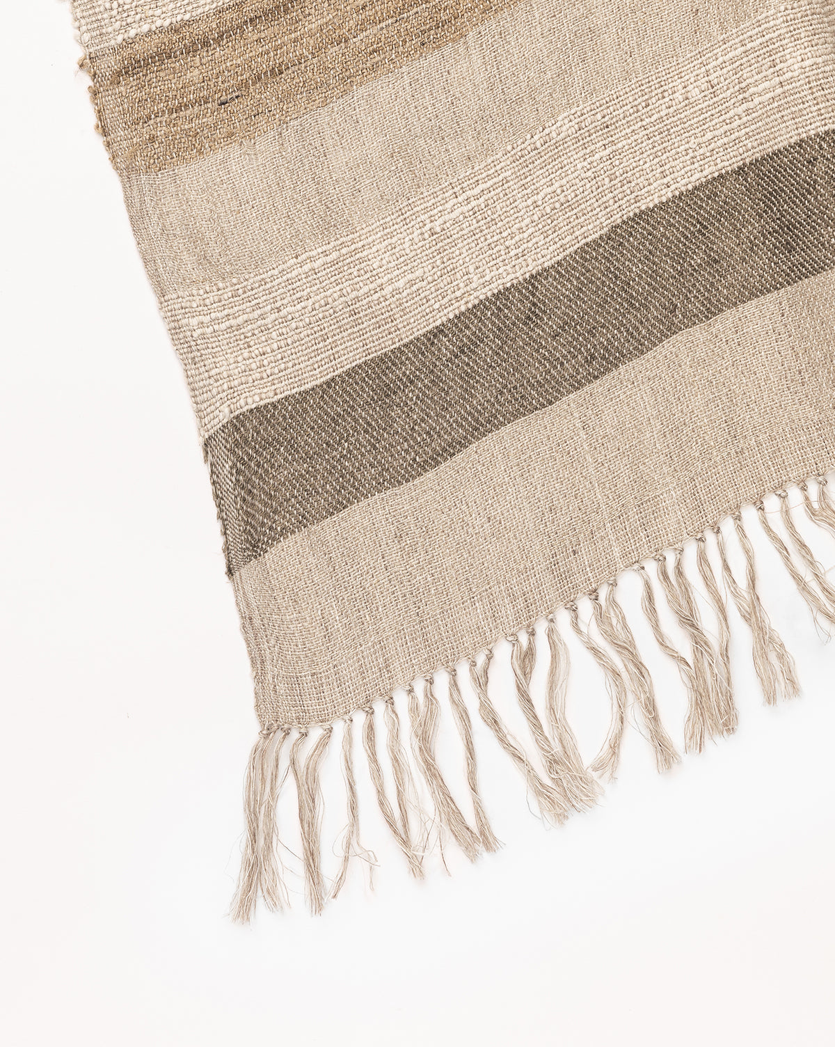 A close-up of the Ashwood Throw, a decorative sofa accessory with horizontal beige and brown stripes and fringed tassels along the bottom edge, set against a white background.
