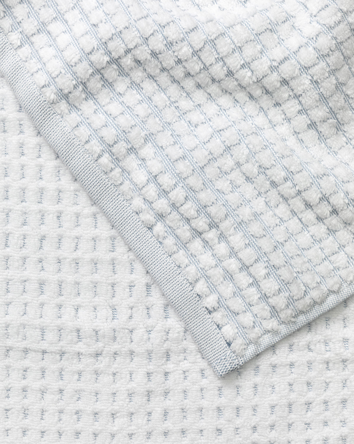 Close-up of a light gray waffle weave towel with a textured pattern and neat edge, displayed on a matching surface—part of our Atrani Gray Organic Bath Collection, by McGee & Co.