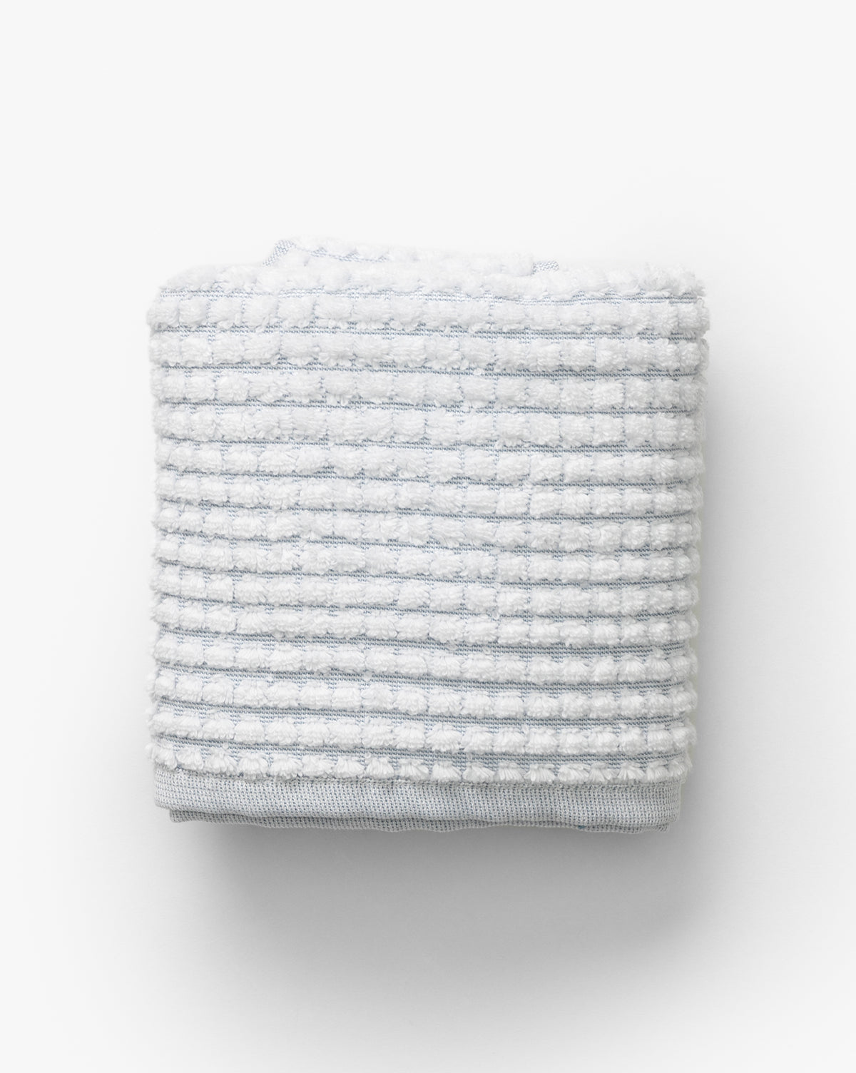 A neatly folded light gray waffle weave towel with a grid pattern from our Atrani Gray Organic Bath Collection, shown against a plain white background by McGee & Co.