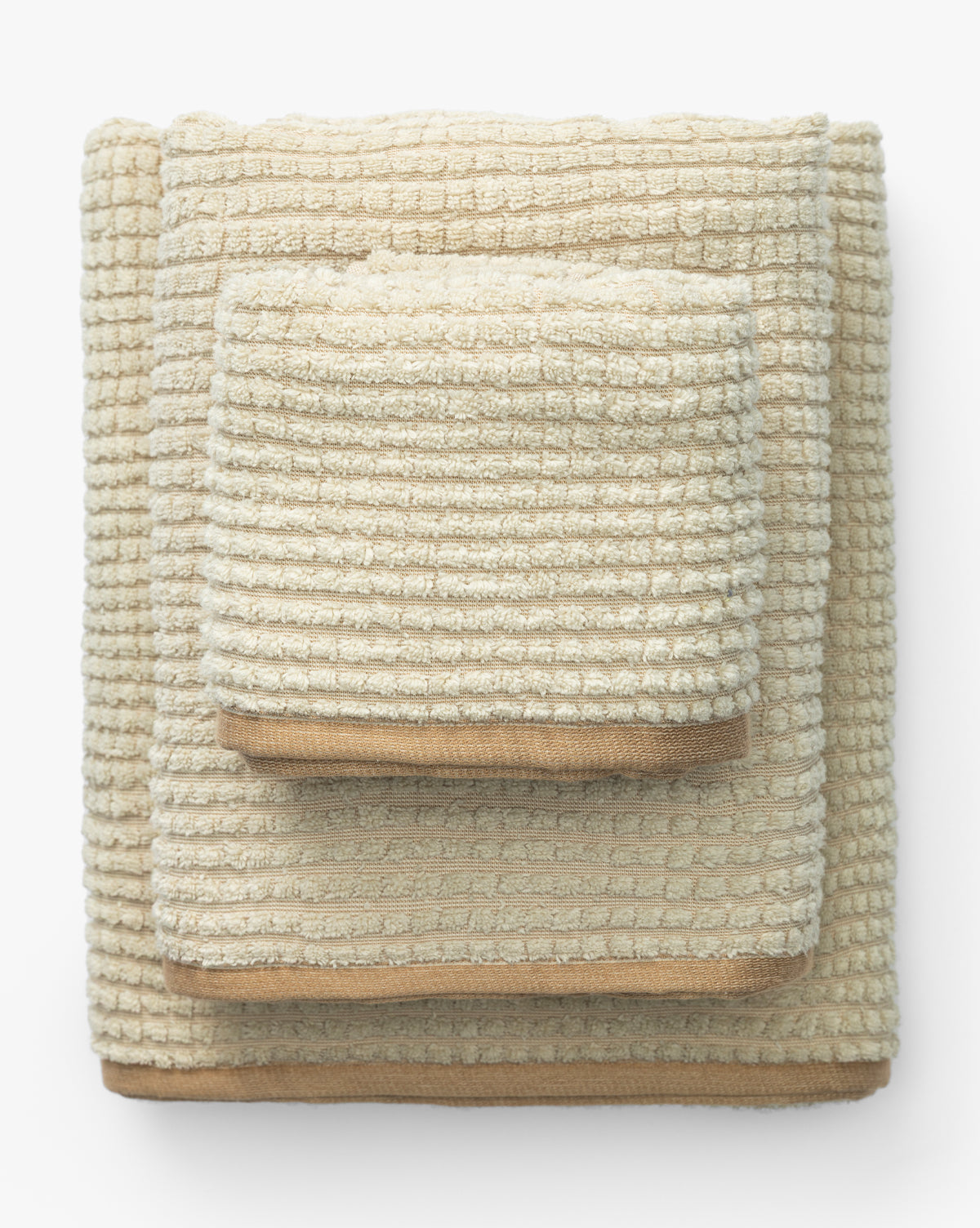 A neatly stacked set of three beige organic cotton towels from the Atrani Organic Bath Collection, featuring a textured waffle weave, arranged largest to smallest on a white background, by McGee & Co.