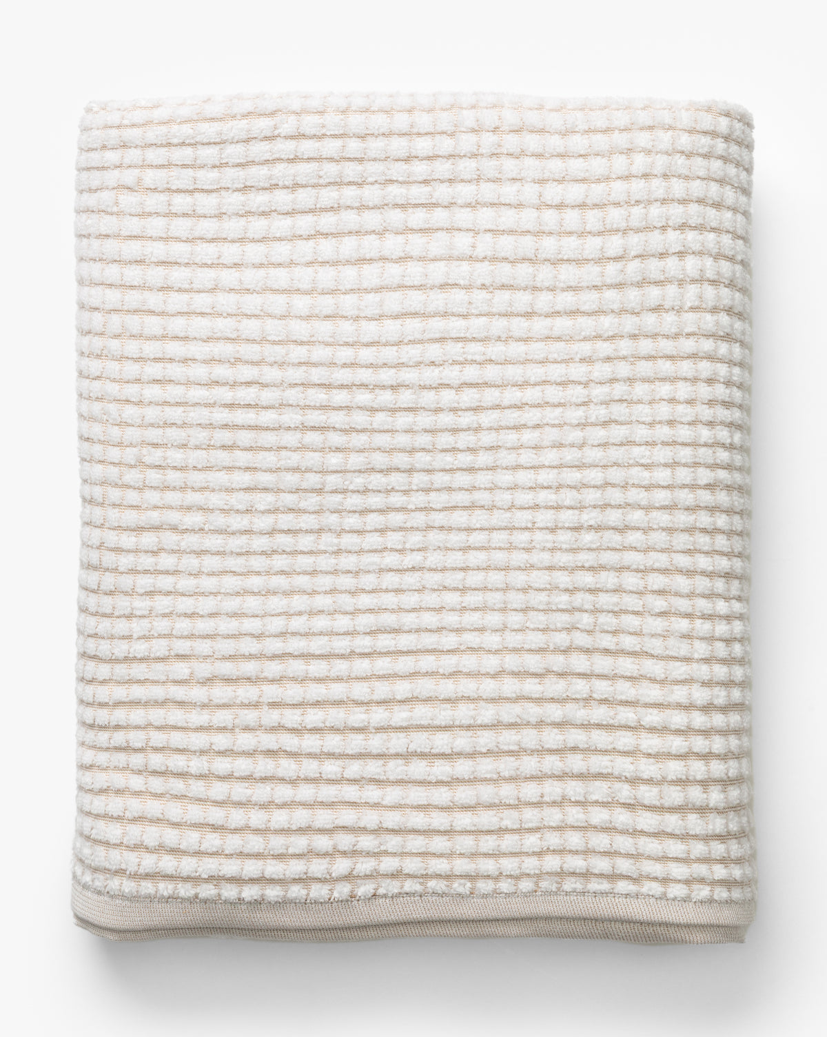 A neatly folded towel from the Atrani Tan Organic Bath Collection, featuring a beige and white checkered waffle weave in soft, textured organic cotton, displayed on a white background by McGee & Co.