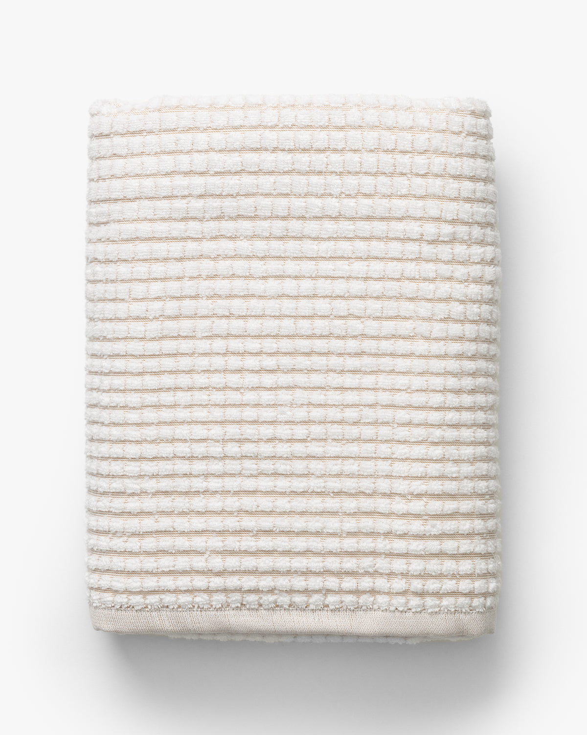 The Atrani Tan Organic Bath Collection features a neatly folded, cream-colored waffle weave towel made from organic cotton with a textured, ribbed pattern, displayed on a white background, by McGee & Co.