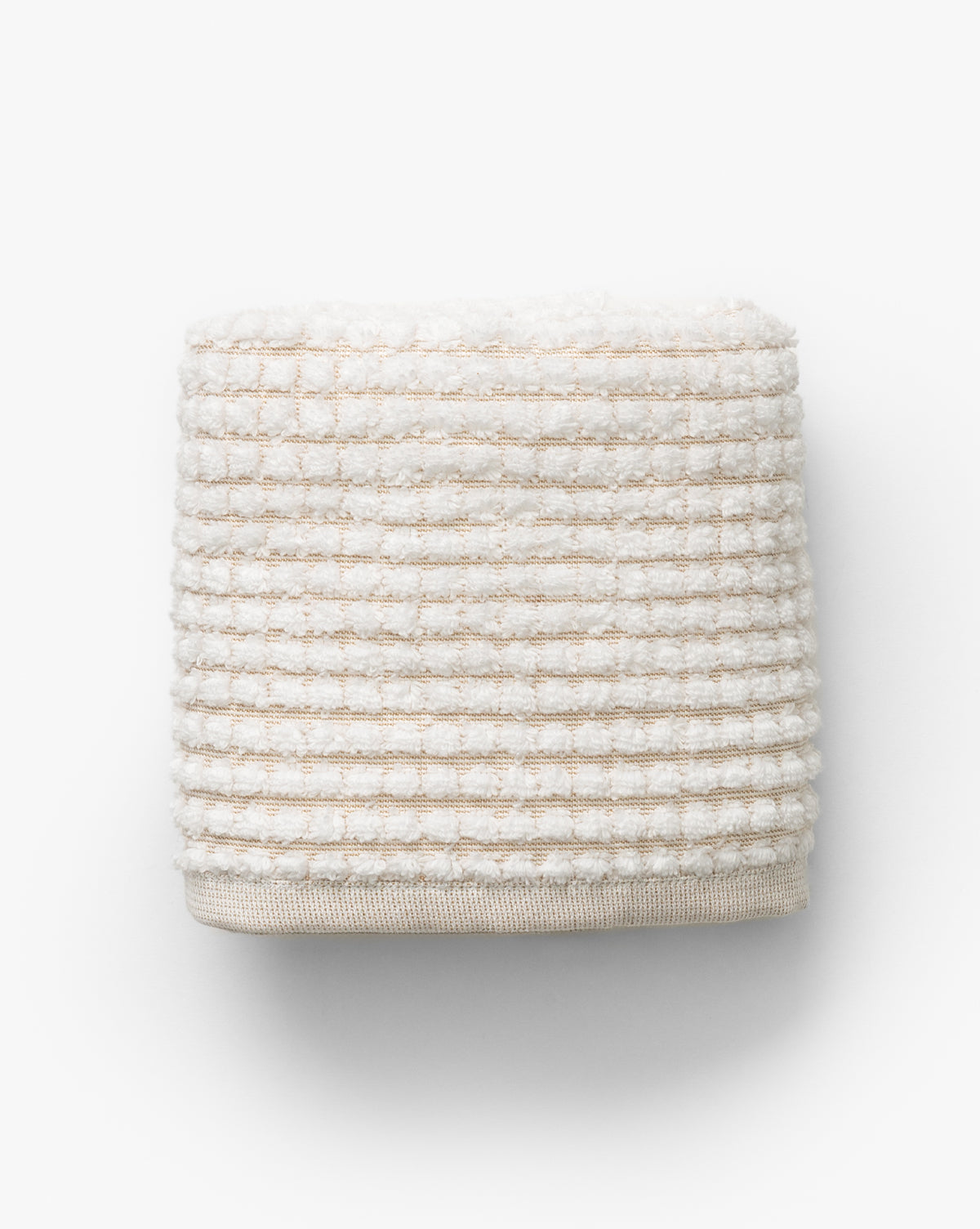 A neatly folded towel from the Atrani Tan Organic Bath Collection, featuring an off-white waffle weave with textured stripes, made from organic cotton and set against a plain white background, by McGee & Co.