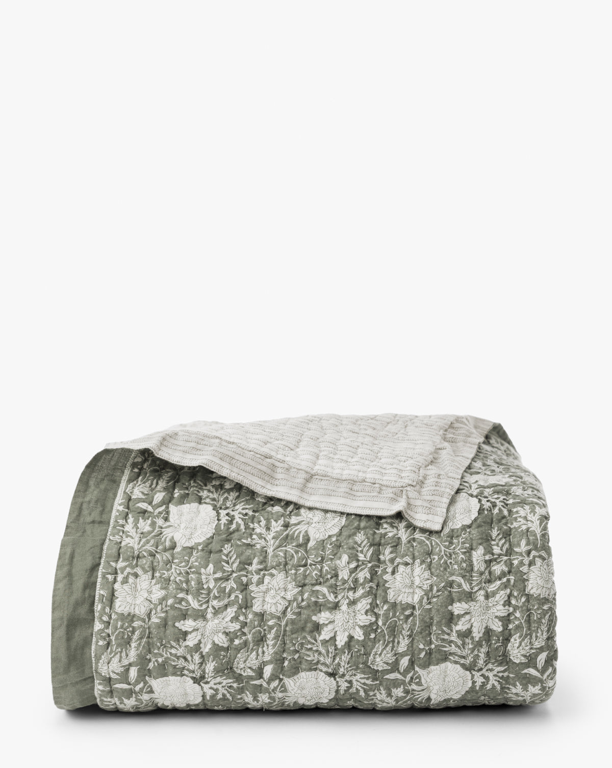 The Audrey Sage Block Print Quilt, featuring a green and white floral pattern with subtle ruffle edging, is folded and topped with a beige textured blanket against a plain white background, by McGee & Co.