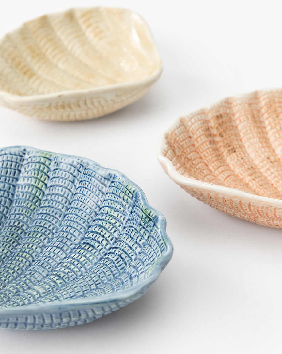 The Aurelie Shell Shaped Bowls (Set of 4) feature coastal-inspired stoneware with a ridged, woven texture. The set includes blue, light yellow, and peach bowls, adding seaside charm to your table by McGee & Co.