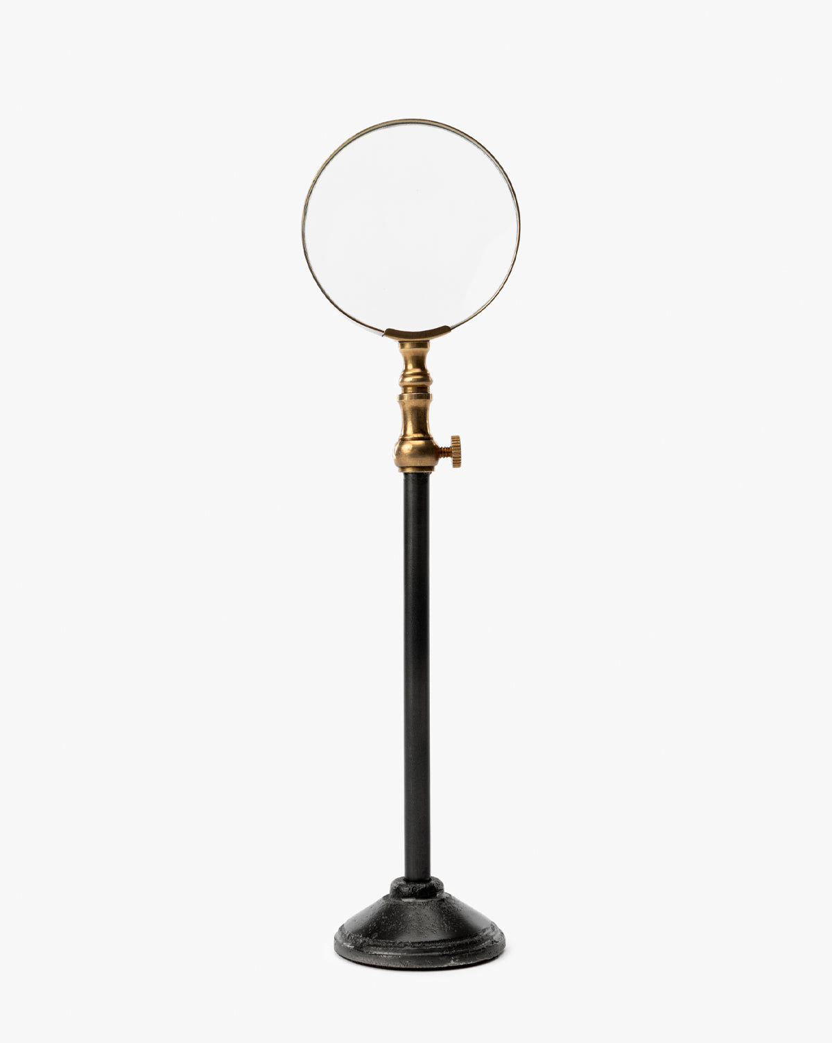 The Barnabas Standing Object features a magnifying glass with a burnished brass holder on a sleek black metal stand, making it an eye-catching piece of home decor against a plain white background, by McGee & Co.