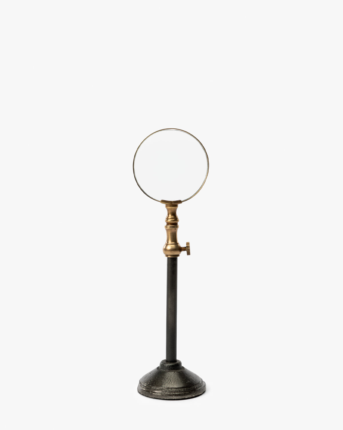 The Barnabas Standing Object features a vintage round lens, burnished brass holder with adjustable knob, and tall black metal stand with a heavy circular base—an elegant home decor piece displayed against a white background, by McGee & Co.