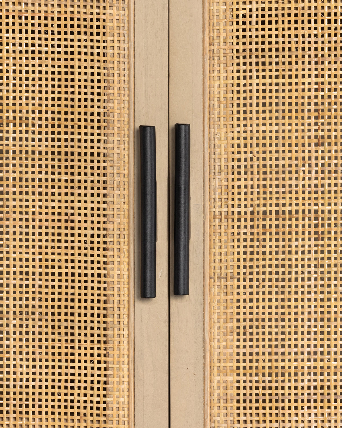 Close-up of two black handles on the Barney Cabinet, a black-washed wood piece with light cane doors. The vertical handles are centered, accentuating the cabinets modern design and woven rattan panel detail, by McGee & Co.