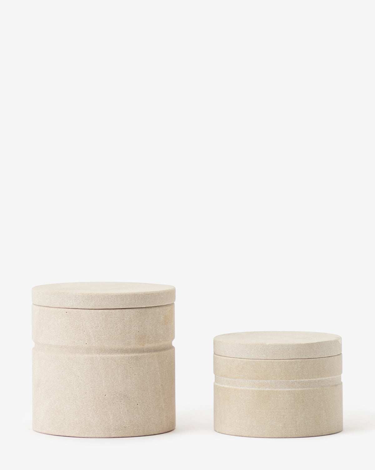 Two round Barton Sandstone Canisters, one large and one small, with lids in beige sandstone are placed side by side on a white background—ideal as a stylish bathroom countertop accent.