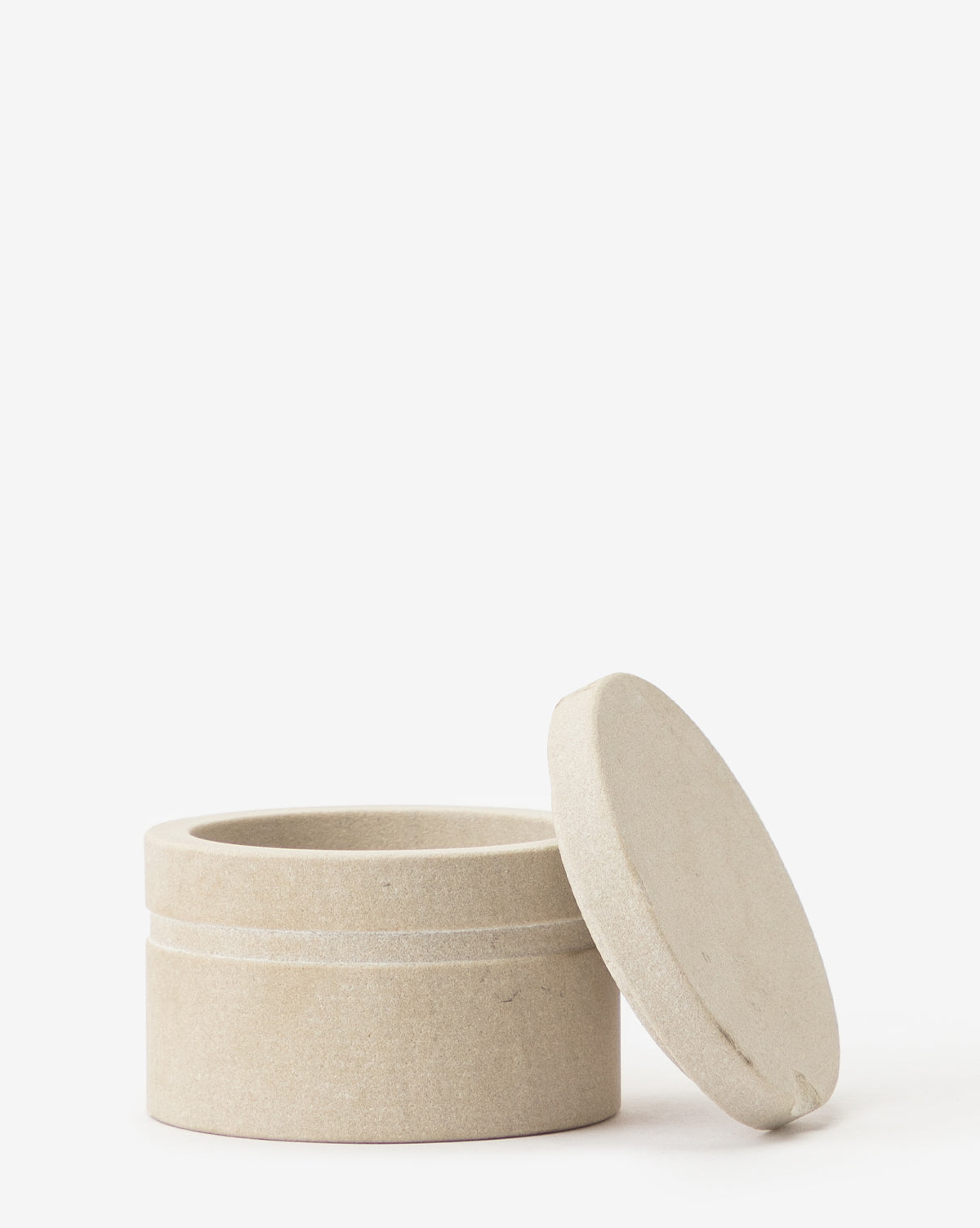 The Barton Sandstone Canister, round and beige with a matching lid set at an angle beside it, sits against a white background—an ideal decorative accent for bathroom countertops.