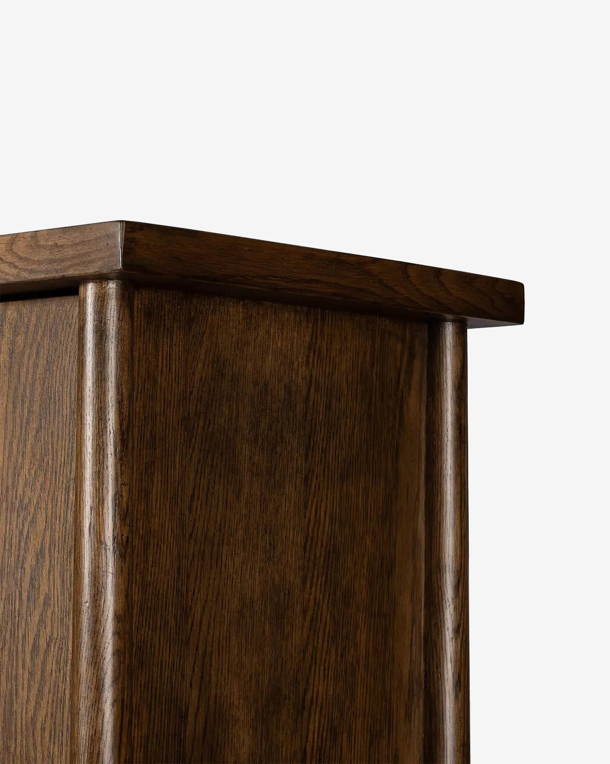 Close-up of the top corner of the Beasley 3-Door Cabinet in dark toasted oak, showcasing its smooth finish and visible wood grain against a plain white background, by McGee & Co.