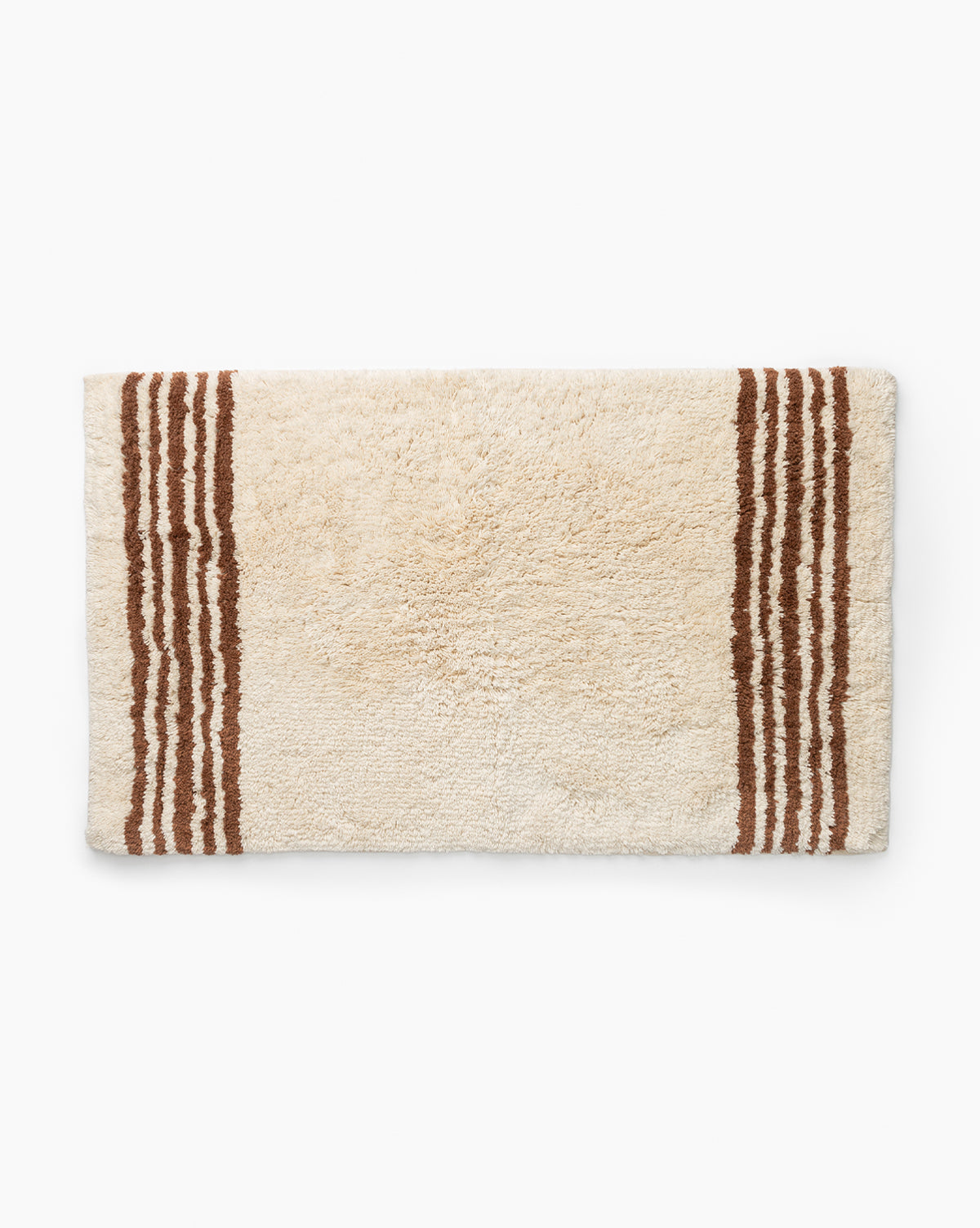 The Beata Bath Mat is a rectangular cream cotton mat with three parallel brown stripes on each short end, shown against a white background.